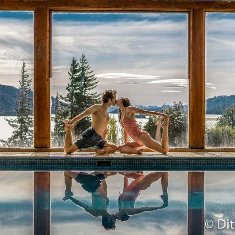 A man and a woman kissing while in a yoga pose next to a pool with a mountain landscape