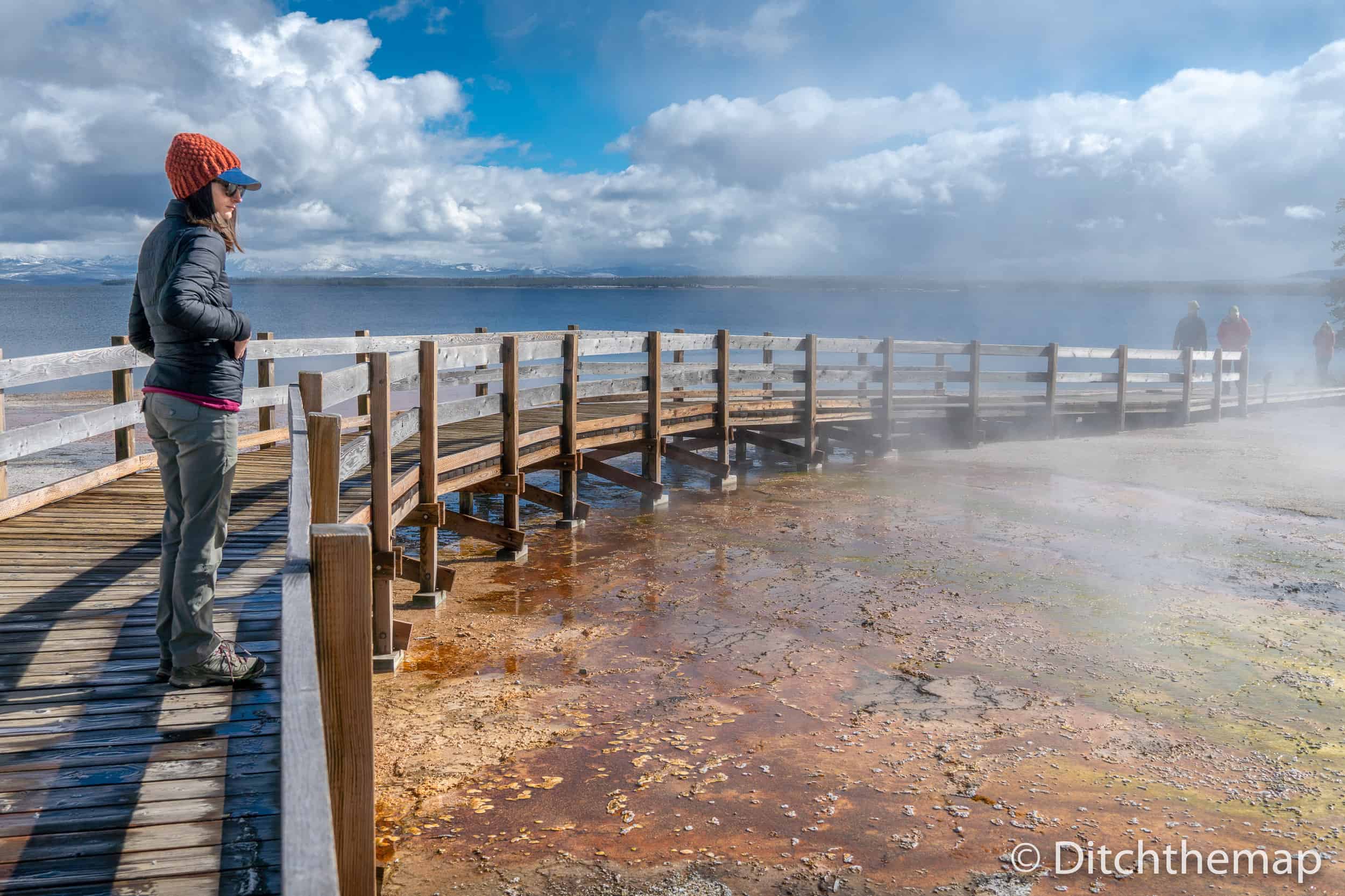 A woman with a jacket looking at the steam coming from the ground at Yellowstone